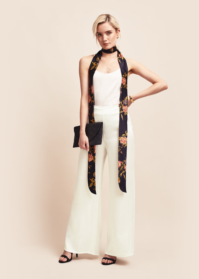 Model wearing pearl off-white silk satin wide leg flare trousers with matching camisole and floral silk tie scarf & black clutch bag.